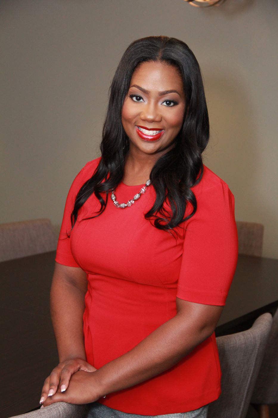 Jocelyn Dena’e in a red top, smiling, resting her hands on a chair